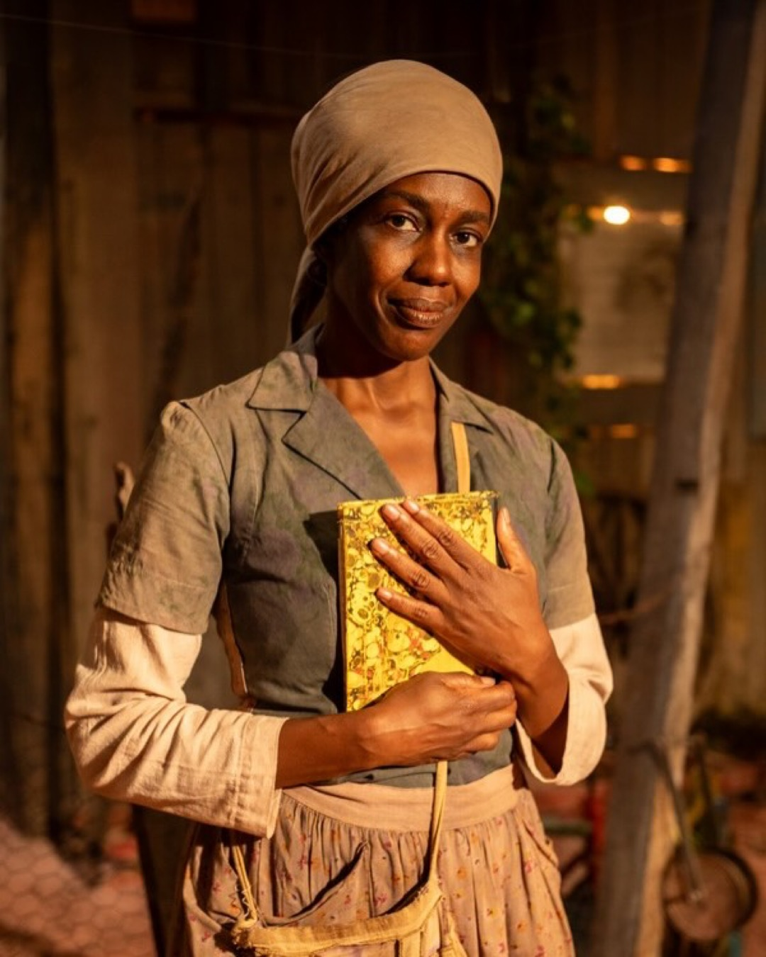 Maria Gal como Carolina Maria de Jesus, segurando um livro com vestimenta de época