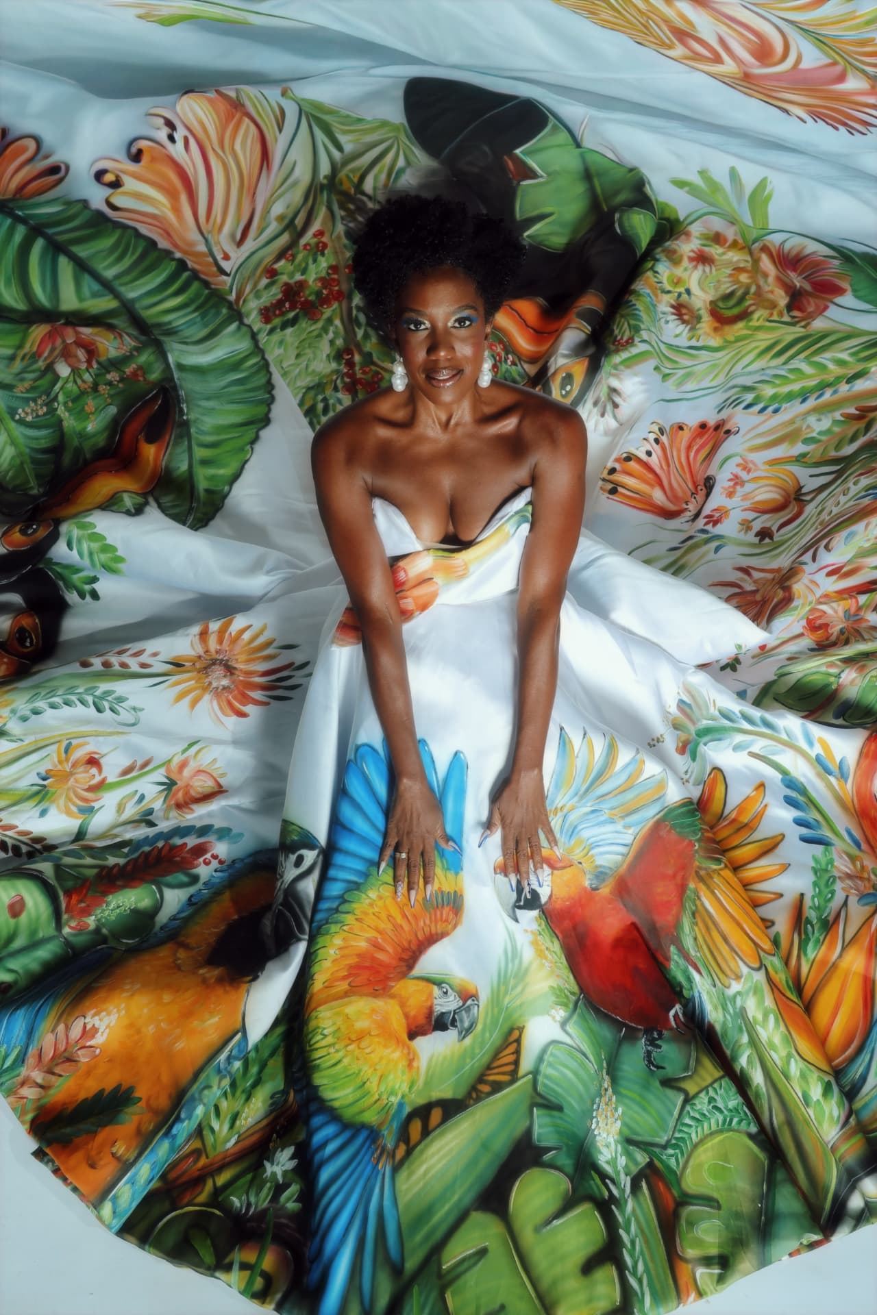 Maria Gal deitada sobre um vestido branco com estampa tropical pintada à mão
